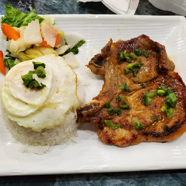 Vietnamese grilled pork chop with a fried egg, rice, and pickled vegetables on a white plate.