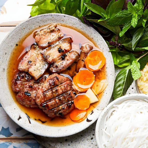 Grilled pork and patties in broth with carrots, served with fresh herbs and rice noodles.