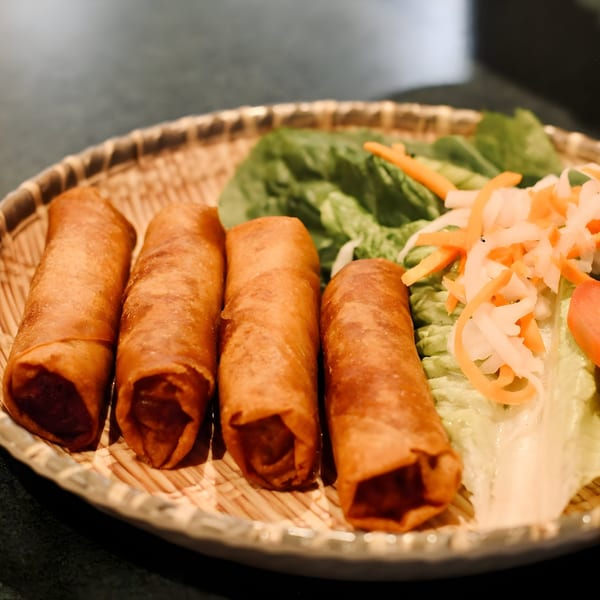 Four crispy Vietnamese fried spring rolls with lettuce, pickled carrots, and daikon on a woven plate.