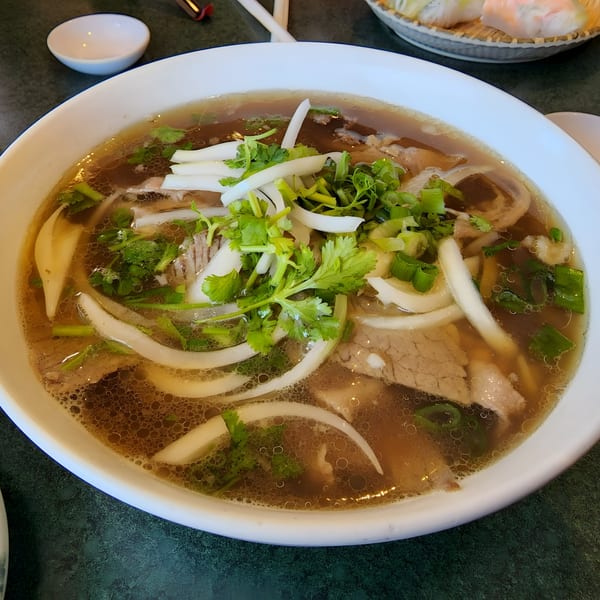 Close-up of a large bowl of Pho Thanh's Vietnamese pho with beef, noodles, and fresh herbs.