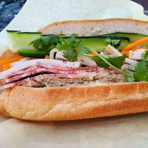 Close-up of a Vietnamese banh mi sandwich with various meats, cucumbers, carrots, and cilantro.