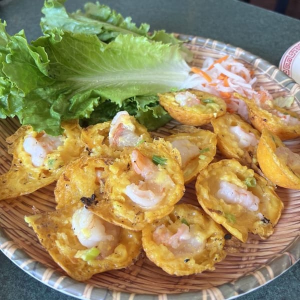 A platter of Vietnamese Banh Khot, crispy mini pancakes with shrimp, served with lettuce and pickled vegetables.